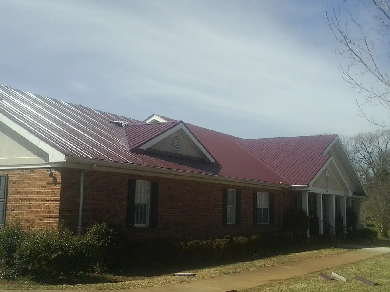 Red metal roof with gabled entries on a long brick building, from a Hail Damage Roof Repair job in South El Monte