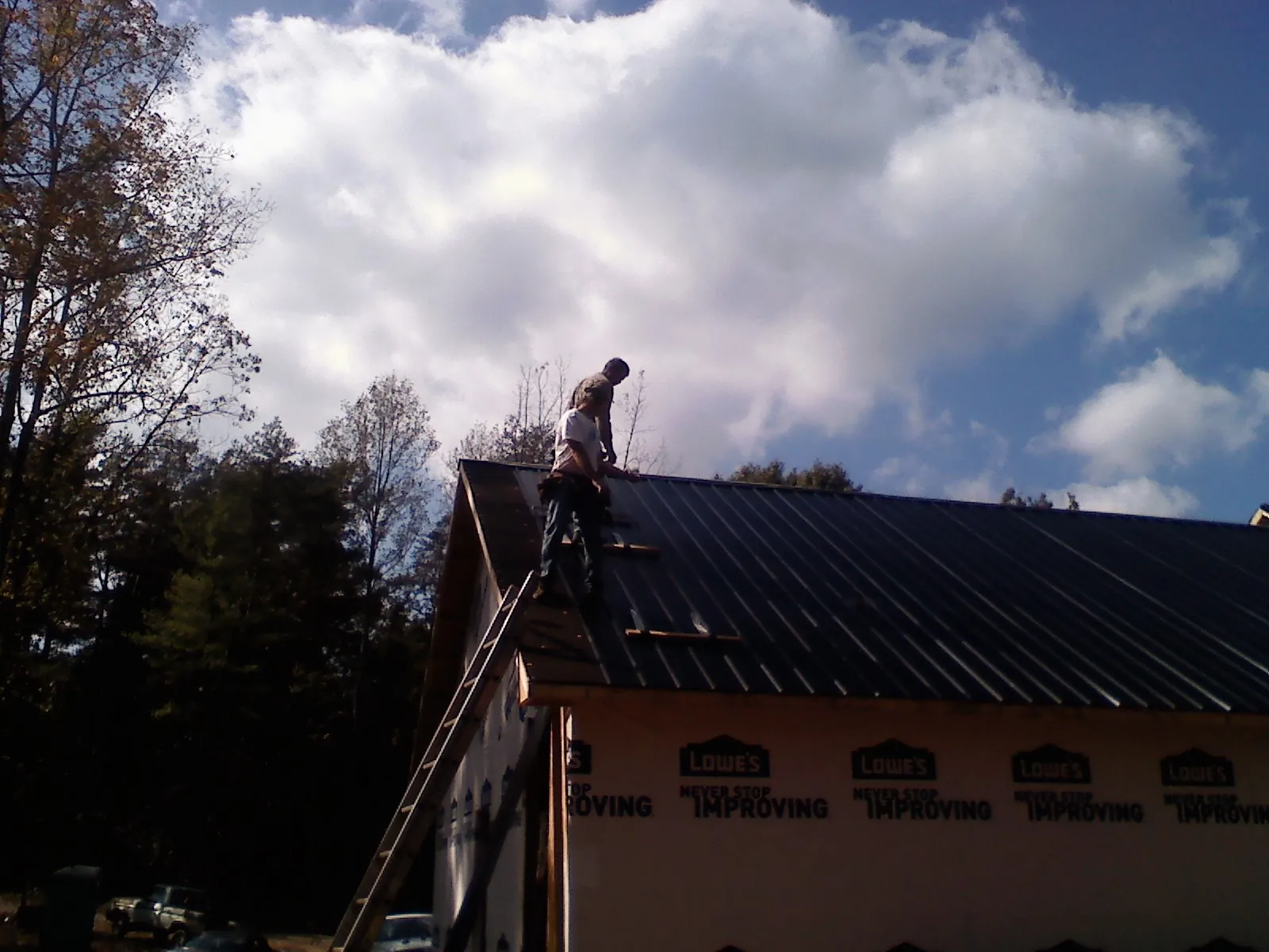 Roofer fastening dark metal panels high against a cloudy sky, from a Roof Inspection job in South El Monte