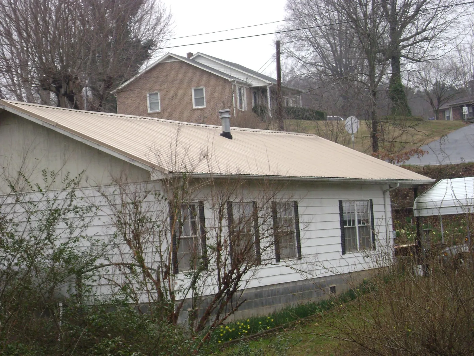 Tan metal roof on a white sided house set into a hillside — Commercial Roofing by Roofing Brothers in South El Monte